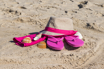 Straw hat, slippers and towel on sand at beach. Accessories for relax in summer