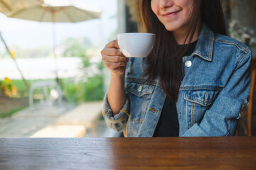 Closeup image of a young woman holding and drinking hot coffee in cafe - 797410074