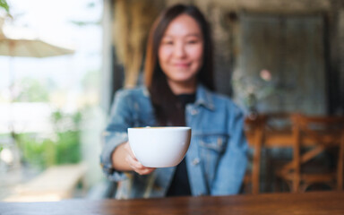 Blurred image of a woman holding and serving a cup of hot coffee in cafe - 797410224