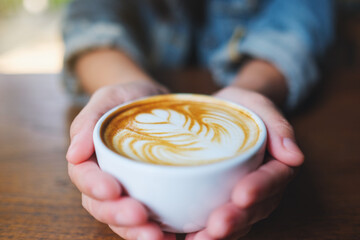 Closeup image of hands holding a cup of hot coffee with latte art - 797410240