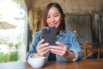Portrait image of a young woman holding and using mobile phone in cafe - 797410282