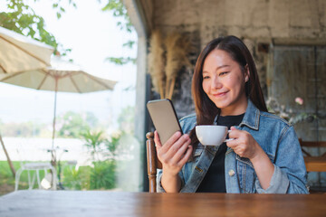 Portrait image of a young beautiful woman holding and using mobile phone while drinking coffee in cafe - 797410420