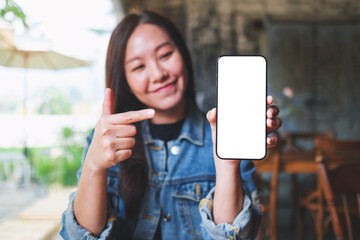 Mockup image of a young woman holding, showing and pointing finger at a mobile phone with blank white screen - 797410857