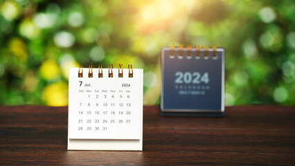 white paper desk calendar for July 2024 on wood table with blurred bokeh background.
