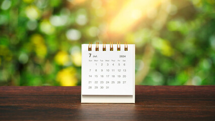 white paper desk calendar for July 2024 on wood table with blurred bokeh background.