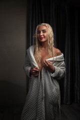 Portrait of a young beautiful blonde girl in a robe in a dark room.
