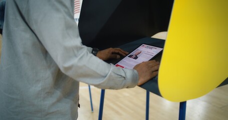 US citizen uses tablet computer for voting. African American man, male voter makes choice and votes in voting booth at polling place. Presidential Election in the United States of America. Civic duty.