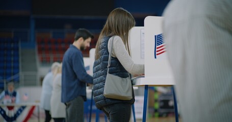 Caucasian female voter comes with bulletin to voting booth. American citizens come to vote in...
