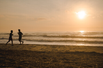 silhouette two man run on beach with sunrise and sea background