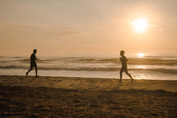 silhouette two man run on beach with sunrise and sea background