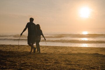silhouette couple walk on beach with sunrise and sea background