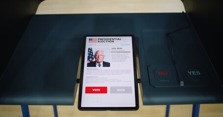 Voting booth at poling station with tablet computer. Information about US presidential candidate and voting buttons displayed on screen. Modern digital voting technology. Elections in United States.