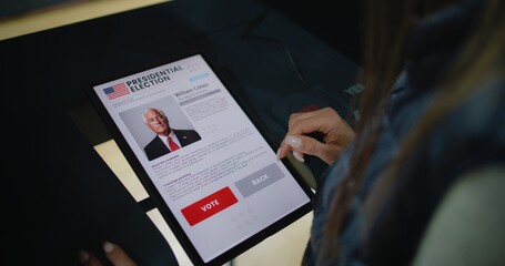 Close up of Caucasian woman making choice and voting for US presidential candidate in voting booth using tablet computer. US citizen at polling station during National Election Day in United States.