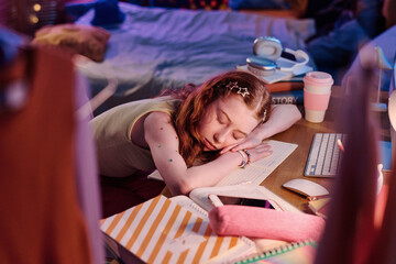 High angle view of tired red-haired girl falling asleep while sitting at desk and doing homework in...