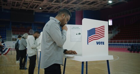African American voter with bulletin comes to voting booth. Diverse American citizens come to vote...