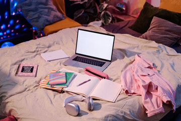 High angle view of laptop, headphones, textbooks and notebooks on bed in teenagers room interior,...
