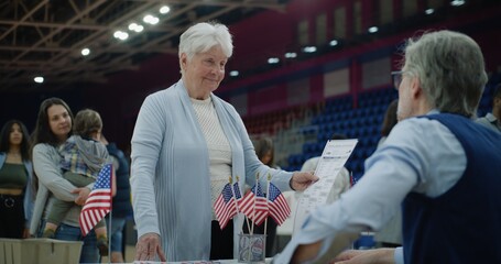 Multi ethnic American citizens come to vote in polling station. Elderly woman talks with polling...