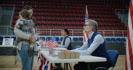 Woman with baby on hands talks with polling officer and takes bulletin. Female American citizen...