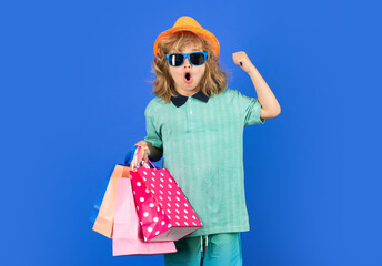 Discounts and sales. Happy Kid boy with shopping bags. Kid with shopping bags posing on blue studio isolated background. Trends and brands.