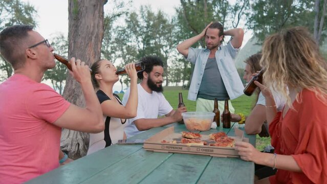 Lively group of friends toasting with beer bottles, sharing a moment of celebration at a sunlit outdoor table, epitomizing the joy of casual gatherings. Slow motion. 