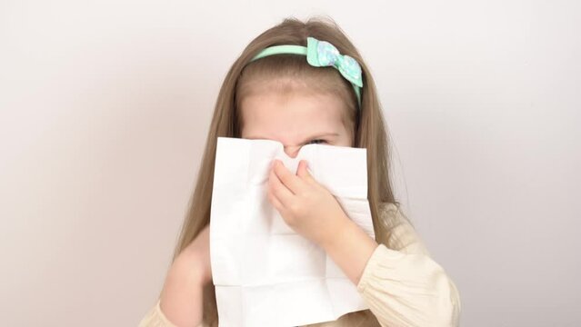 Portrait of a girl blowing her nose with disposable tissues on a white background. Little girl with a runny nose.