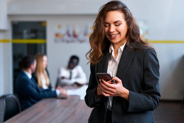 Businesswoman in smart casual attire smiles at smartphone in office setting, team discussion...