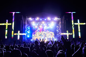 Outdoor religious music festival at night with vibrant stage lights. Excited audience raises hands...