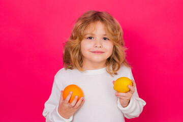 Kid with orange and lemon in studio. Studio portrait of cute child hold lemon and orange isolated on red background.