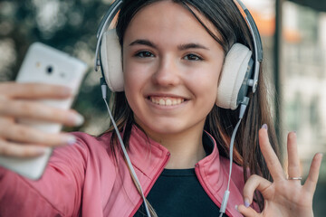 teen girl wearing headphones and making ok sign on the street