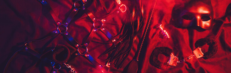 set of BDSM sex toys with handcuffs, whip flogger, butt anal plug for submission and domination on a red background. Wide header cover for banner for sex shop