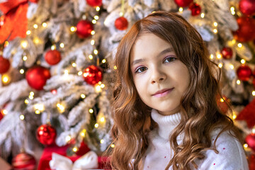 Portrait of a happy girl looking at the camera, posing against the background of a Christmas tree.