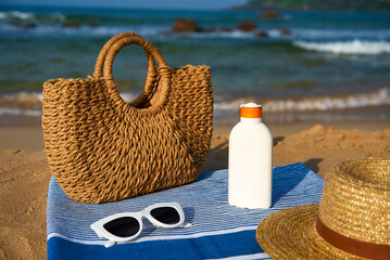 Beach essentials on sandy shore woven bag, white sunscreen bottle, stylish sunglasses atop blue...