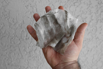 dirt, hairs and grey dust on wet wipes in male hand.  isolated on white wall background.