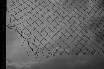 wire net Fence. Blue dramatic, cloudy sky. Wire mesh on background of blue sky and white clouds. black silhouette of  wire fence, metallic net.
