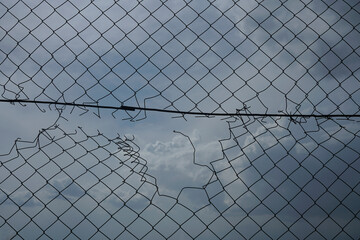 Looking up at a chain link fence with blue sky and clouds. wire fence. Chain link fence see blue...