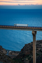 Truck with refrigerated trailer driving along a high viaduct and the sea in the background, vertical photo.