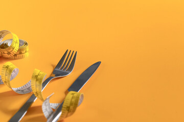 Fork and knife wrapped with measuring tape on yellow background. Weight loss and healthy concept