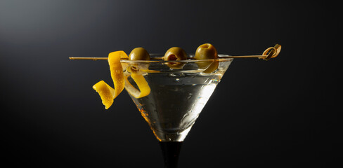 Classic dry martini cocktail with green olives and lemon peel on a black background.