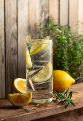 Gin-tonic cocktail with ice, rosemary and lemon slices.