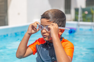 Young boy secures his swimming goggles in a pool with a blue swim cap.