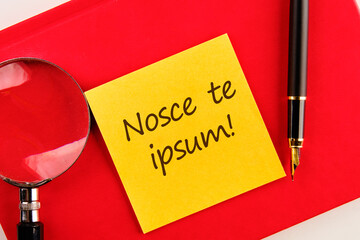 Latin proverb NOSCE TE IPSUM (know yourself) on a yellow sticker on a red notebook