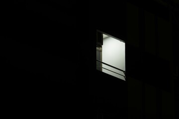 A window in a building is lit up by a light. The window is small and the light is shining through...