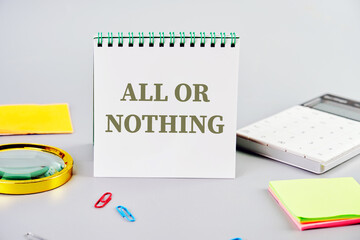 All or nothing, motivational phrase written on a notepad on a gray background next to office supplies