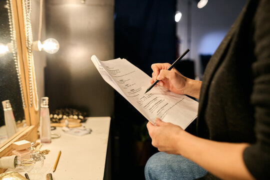 Close up of unrecognizable actress reading script backstage and taking notes copy space