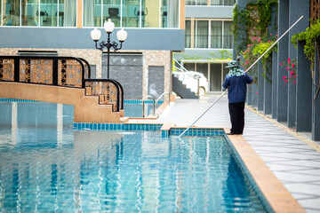 Staff are cleaning the hotel pool using an underwater vacuum pump.