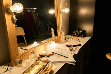 Close up of cluttered vanity table backstage with make up and script papers lit by warm lamp light...