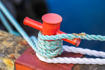 A red mooring bollard on a pier with ropes