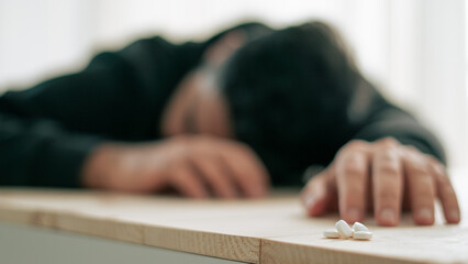 Depressed man committing suicide. A lot of pills spilled on table.