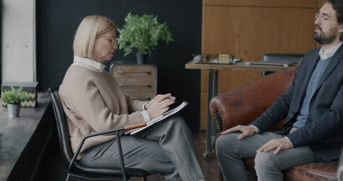 Middle Eastern man talking to female therapist discussing business problems indoors in modern office. Professional therapy and psychology concept.
