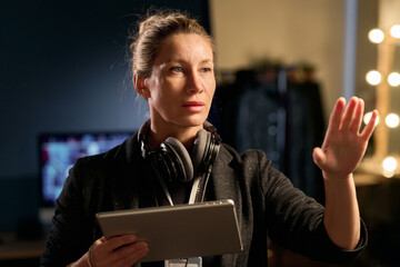 Waist up portrait of adult female director giving instructions and gesturing on set and holding...